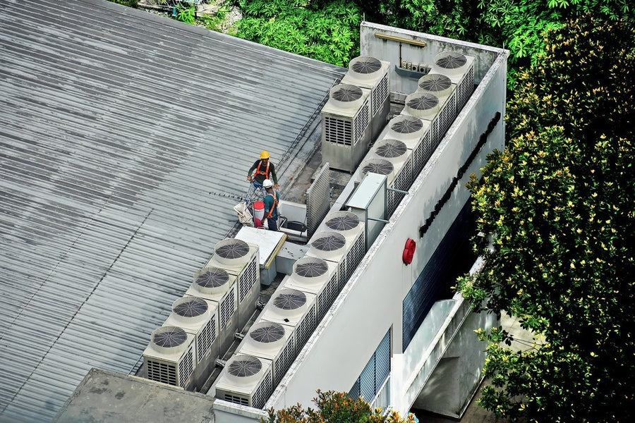 Técnicos con casco revisando las unidades de climatización en la cubierta de un edificio